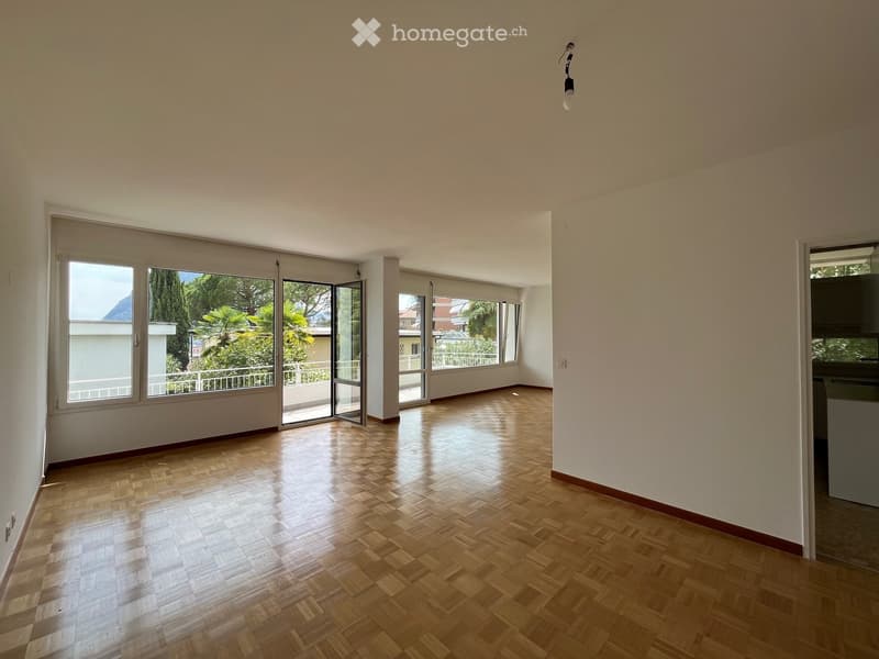 Empty room with wooden herringbone flooring, large windows, and sliding glass doors leading to a balcony.