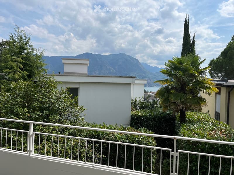 Balcony overlooking a lush garden with a palm tree, surrounded by greenery and a scenic mountain view in the background.