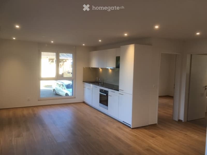 Modern kitchen with white cabinets, a sink, an oven, and a faucet, featuring wooden flooring and large windows.