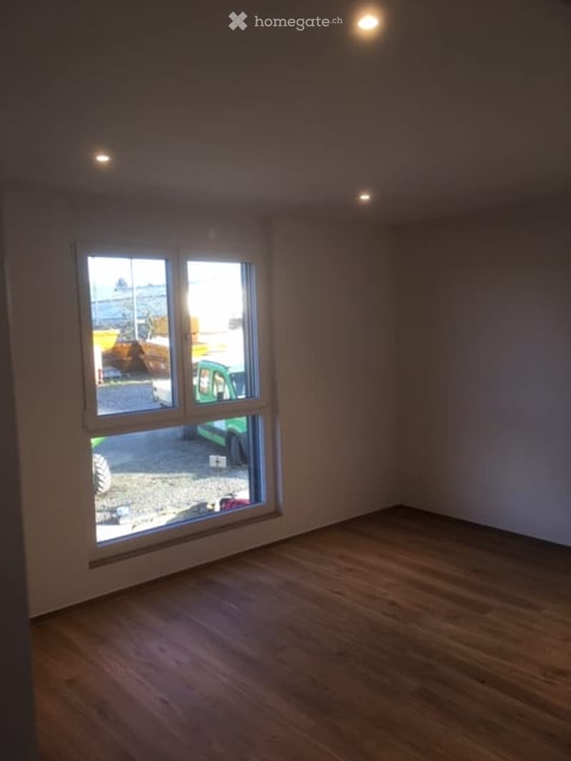 Empty room with wooden flooring and large window showing outdoor view. No furniture or equipment present.