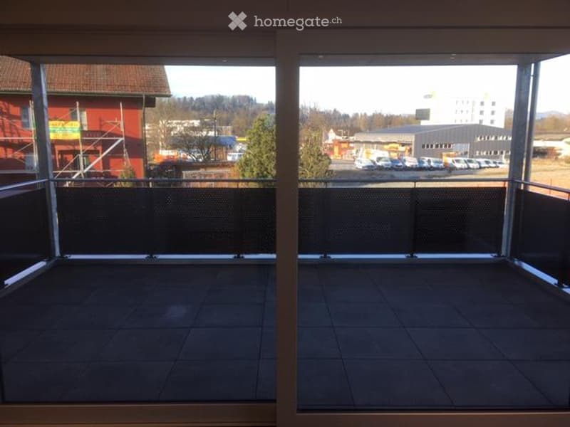 Modern balcony with dark tiled flooring, metal railings, and large glass windows offering a view of the surrounding area.