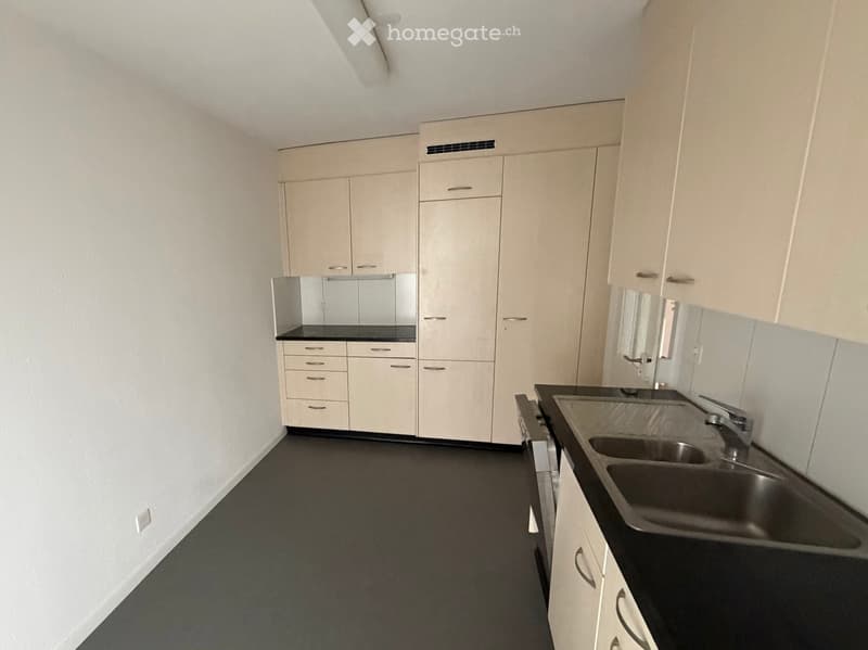 Empty kitchen with white cabinets, black countertops, and a stainless steel sink.