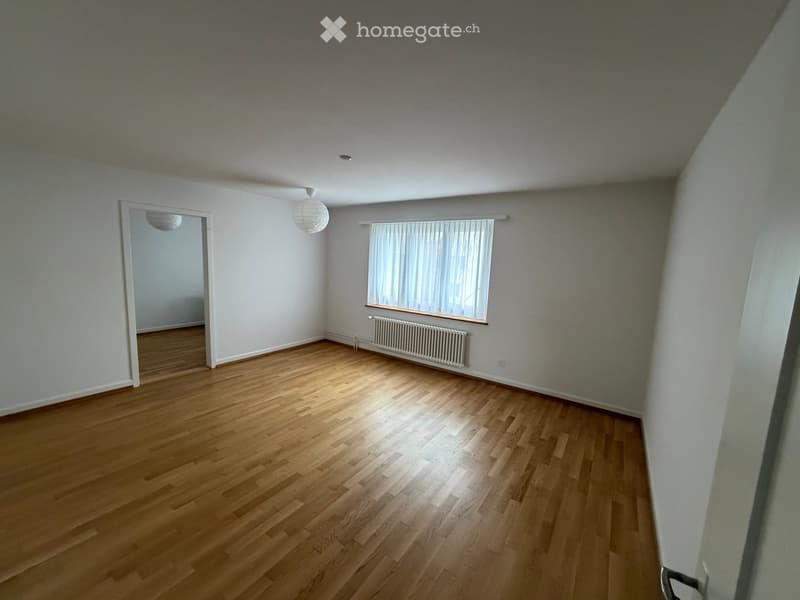 Empty room with wooden flooring, white walls, a window with blinds, a radiator, and a doorway leading to another space.