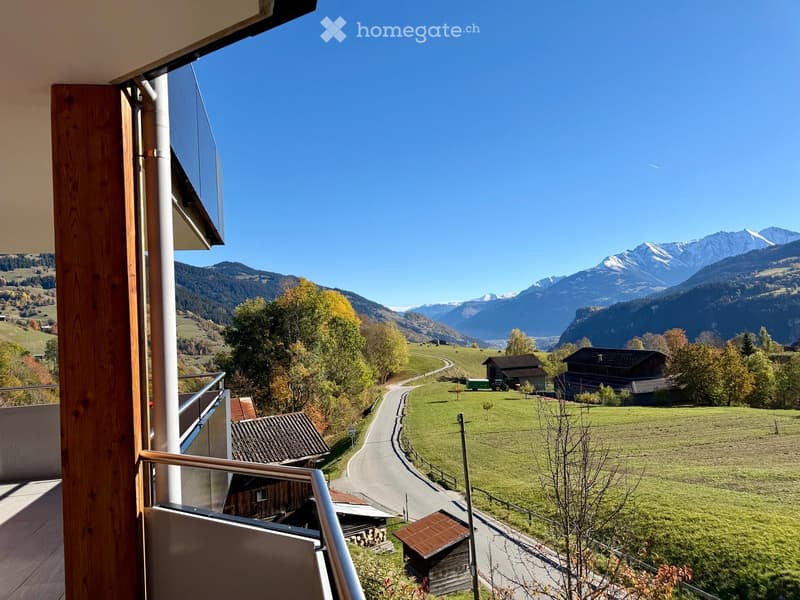 Balcony overlooking a scenic valley with mountains, a winding road, and scattered houses.