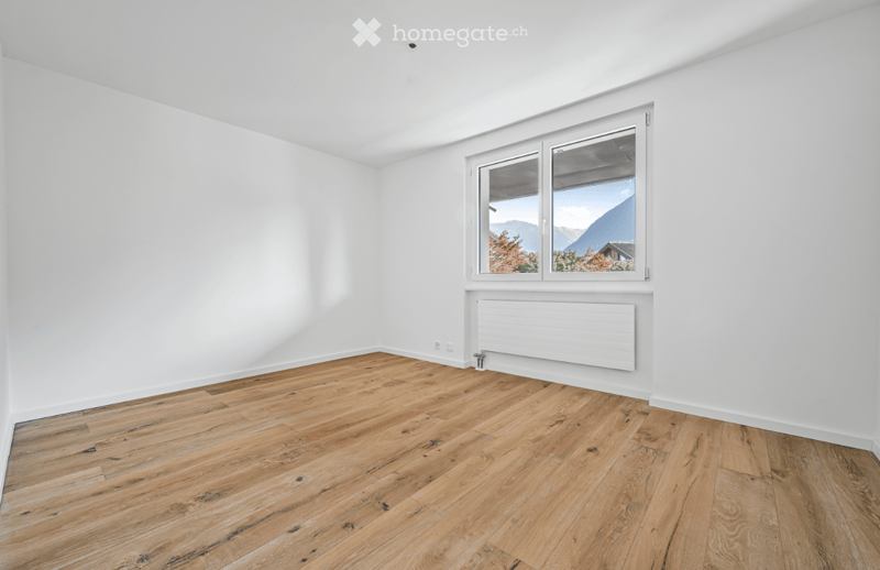 Empty room with white walls, wooden floor, and a large window showing a scenic mountain view.