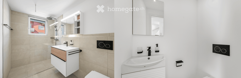 Modern bathroom with a white sink, mirror, toilet, and shower area. Features a sleek design with a wooden cabinet and a large window providing natural light.