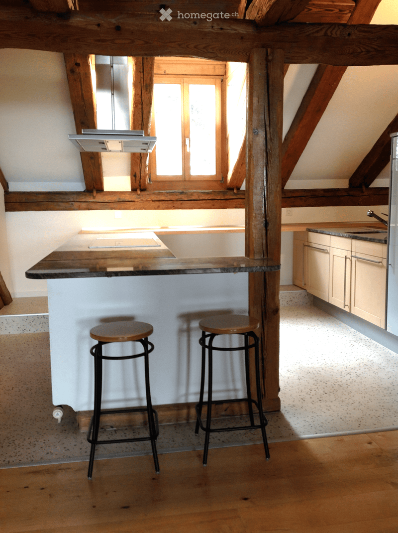 Modern kitchen with wooden beams, a central island with a marble countertop, two stools, and built-in cabinets.