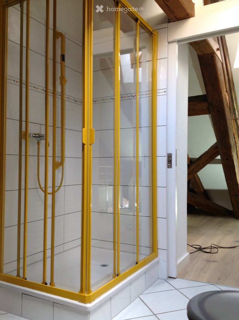 Modern bathroom with a glass shower stall featuring yellow framing, white tiled walls, and a visible faucet.