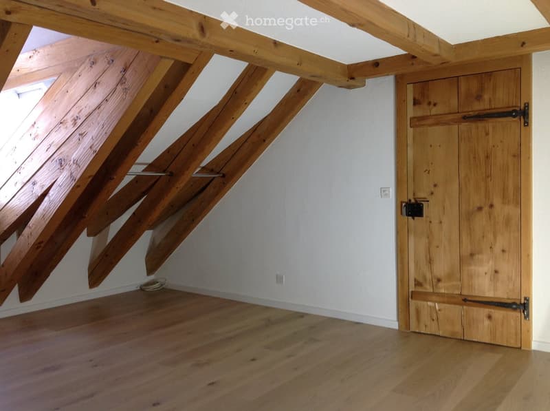 Empty attic space with exposed wooden beams, wooden floor, and a wooden door.