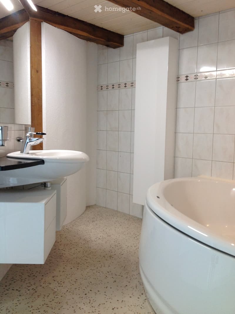 Bathroom with white tiled walls, a white sink with a modern faucet, and a bathtub. The floor has a speckled beige tile pattern.
