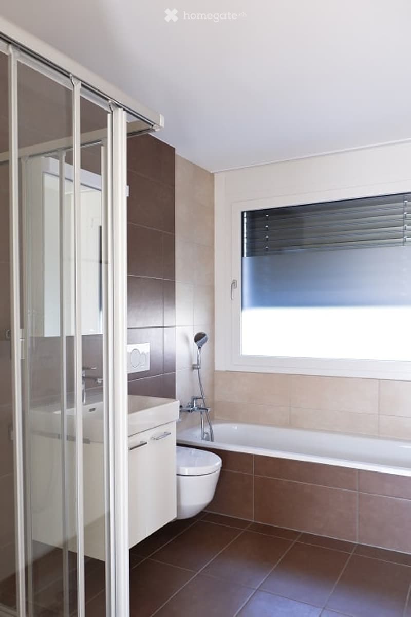 Modern bathroom with a bathtub, glass shower enclosure, white vanity, and tiled flooring.