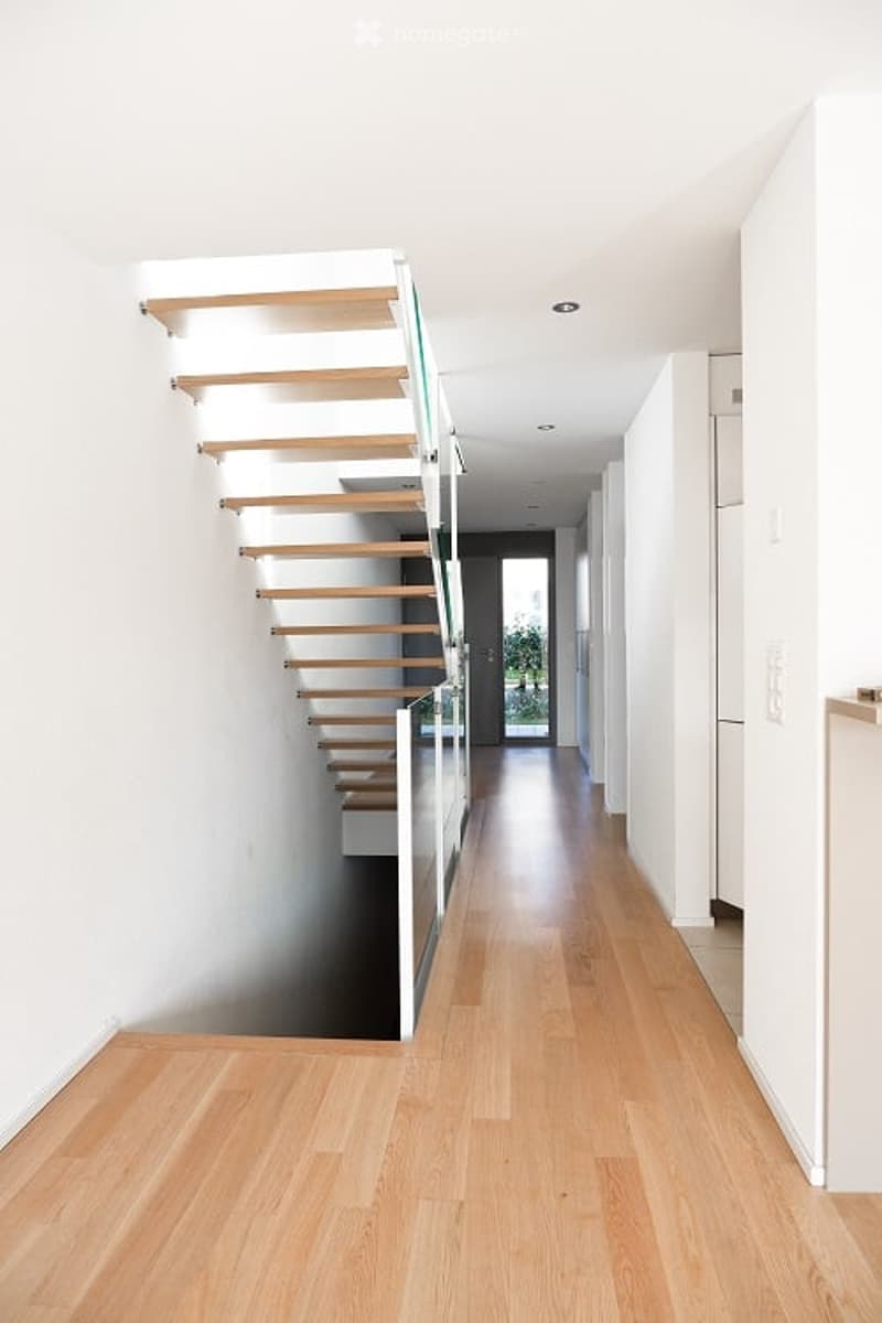 House interior with wooden floor, white walls, modern staircase with glass railing, corridor leading to rooms