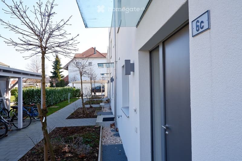 Single family home, modern design, apartment with 6C, paved walkway, bicycles parked, greenery and hedges surrounding the area
