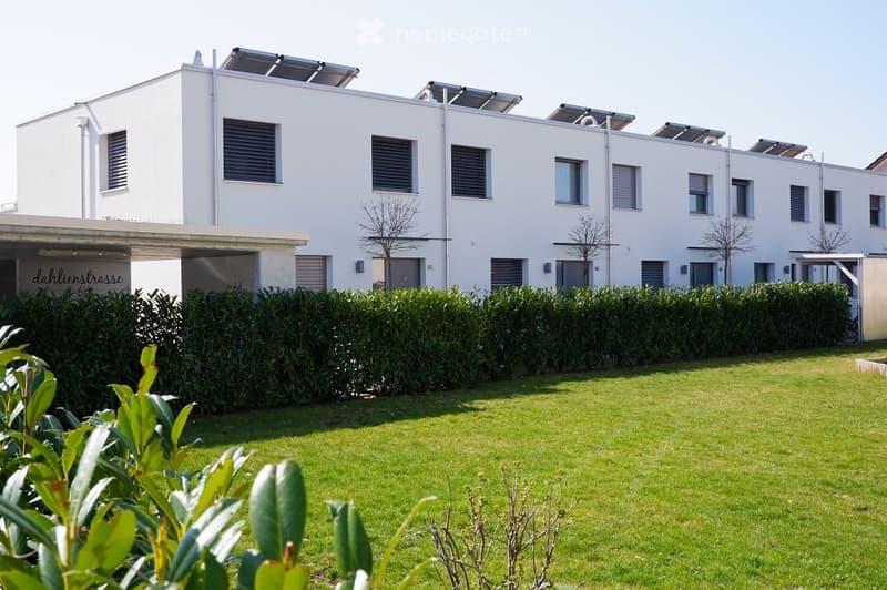 Multi-family residence, white exterior, solar panels on the roof, hedge in front, well-maintained lawn, clear sky