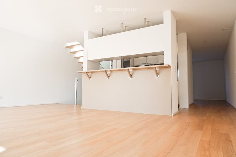 Modern open space, wooden floors, white walls, elevated kitchen area with cabinets and a fridge, and an open staircase.
