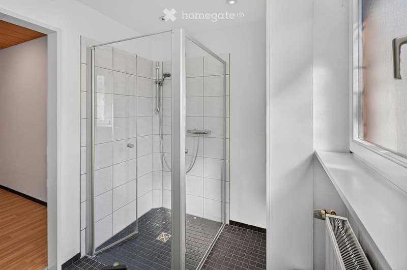 Modern bathroom with a glass-enclosed shower stall, tiled walls, and a radiator beneath a window.