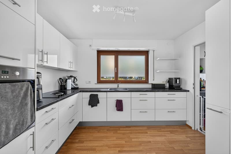 Modern kitchen with white cabinets, black countertops, wooden flooring, and stainless steel appliances. Features include an oven, a sink with a faucet, a coffee maker, and various kitchen utensils.