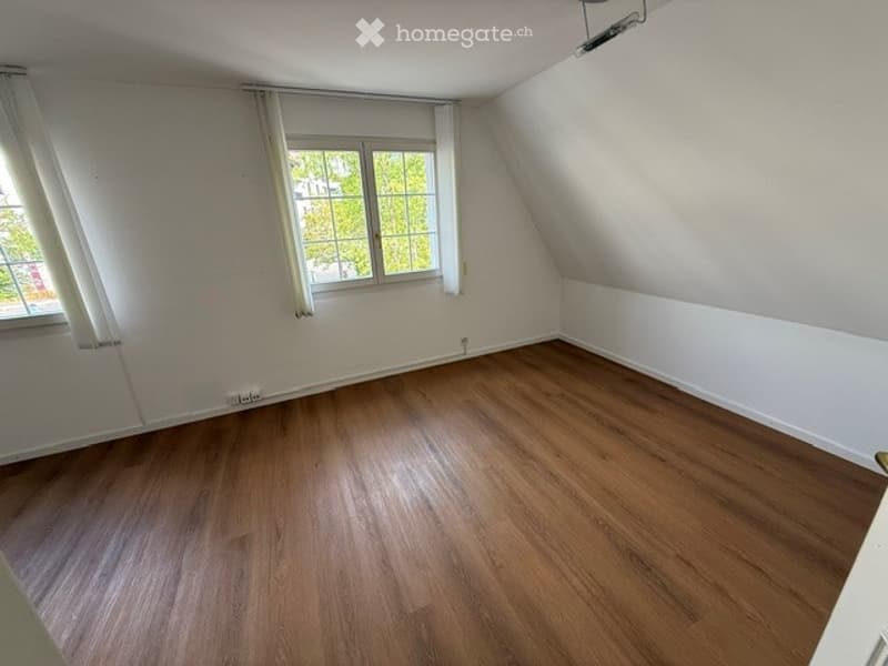 Empty room with wooden flooring, white walls, and large windows with white curtains. No furniture or equipment present.