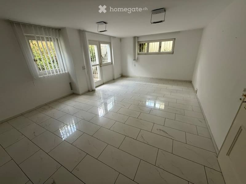 Empty room with white tiled flooring, white walls, and large windows with blinds. No furniture or equipment present.