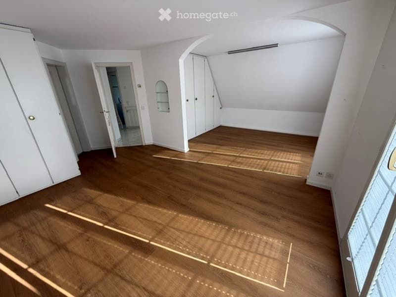 Empty room with wooden flooring, white walls, built-in wardrobes, and a large window allowing natural light to enter.