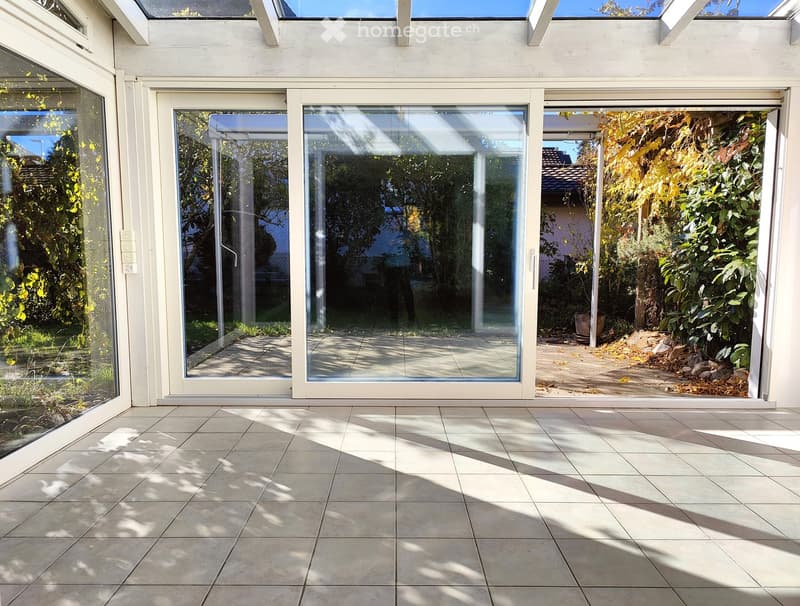Empty room with tiled floor and large sliding glass doors leading to a garden area.