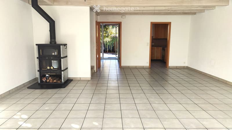 Empty hallway with tiled floor, white walls, and a wood-burning stove on the left side. There are two open doorways leading to other rooms.
