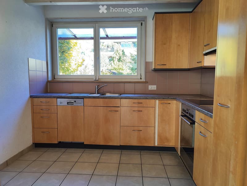 Modern kitchen with light wooden cabinets, tiled walls, and a granite countertop. Features a sink, faucet, dishwasher, and oven.