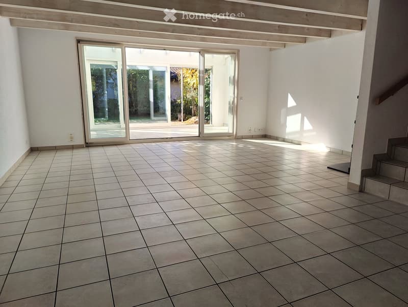 Empty room with tiled floor, white walls, large sliding glass doors leading to an outdoor area, and a staircase visible on the right side.