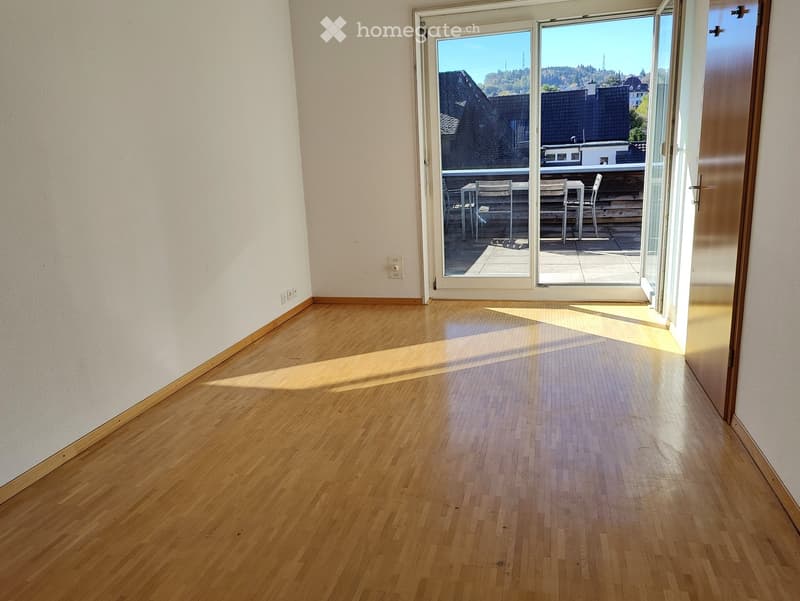 Empty room with wooden flooring and large sliding glass doors leading to a balcony area with outdoor furniture.