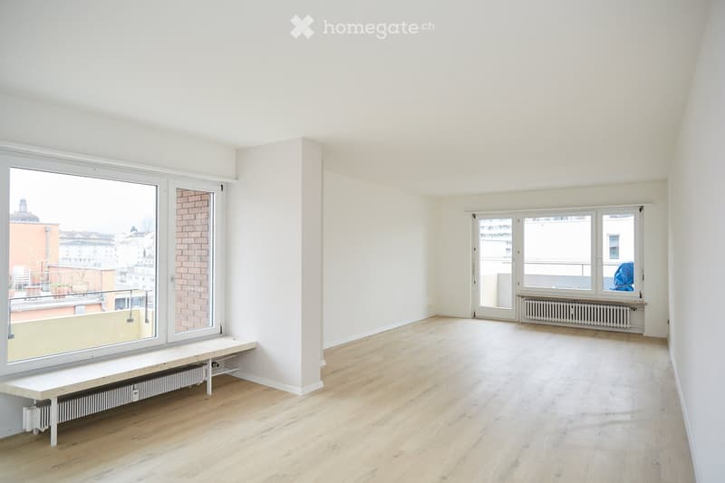 Empty room with light wooden flooring, white walls, large windows, and radiators. No furniture or equipment present.