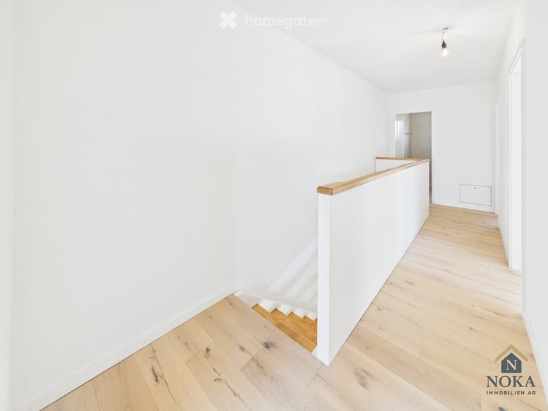 Empty hallway with white walls, wooden flooring, and a staircase leading upwards.