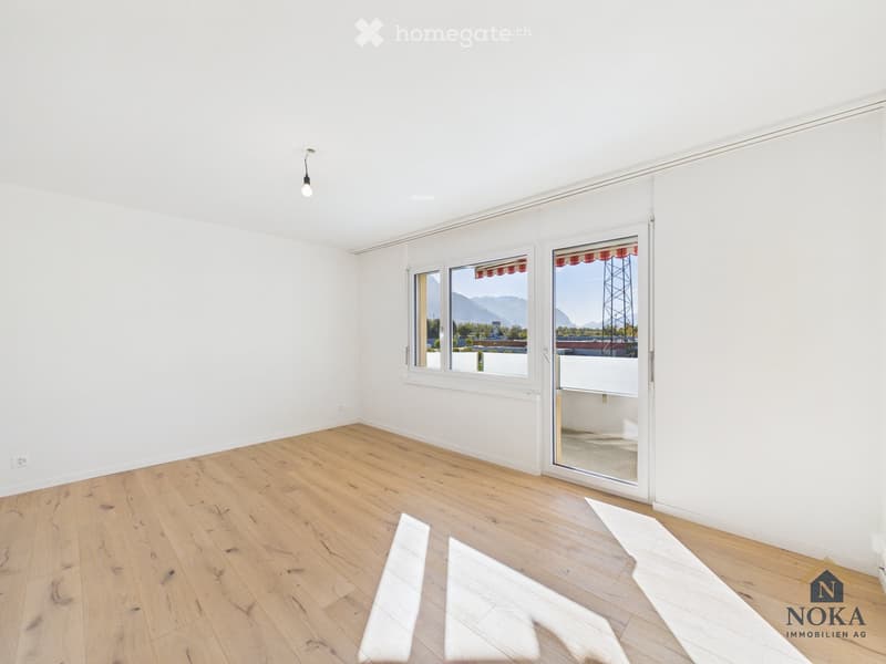 Empty room with white walls, wooden floor, large windows, and a sliding glass door leading to a balcony.