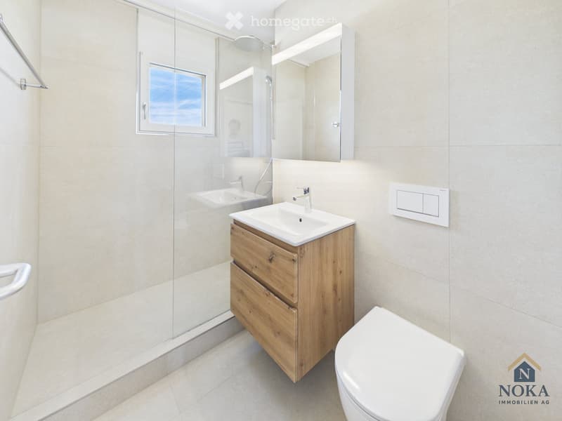 Modern bathroom with a wooden vanity, white sink, toilet, large mirror, and a glass-enclosed shower area.