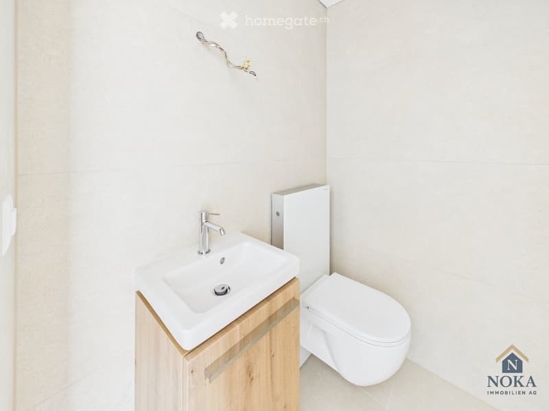 Modern bathroom with a white sink, chrome faucet, and a white toilet. Light-colored tiles and wooden cabinetry.