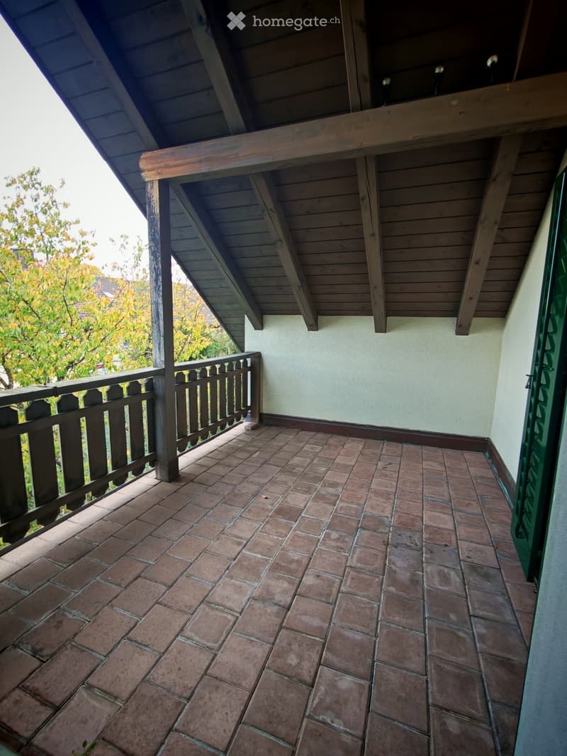 Balcony with brick tiles, wooden railing, and a view of trees and a neighboring house.