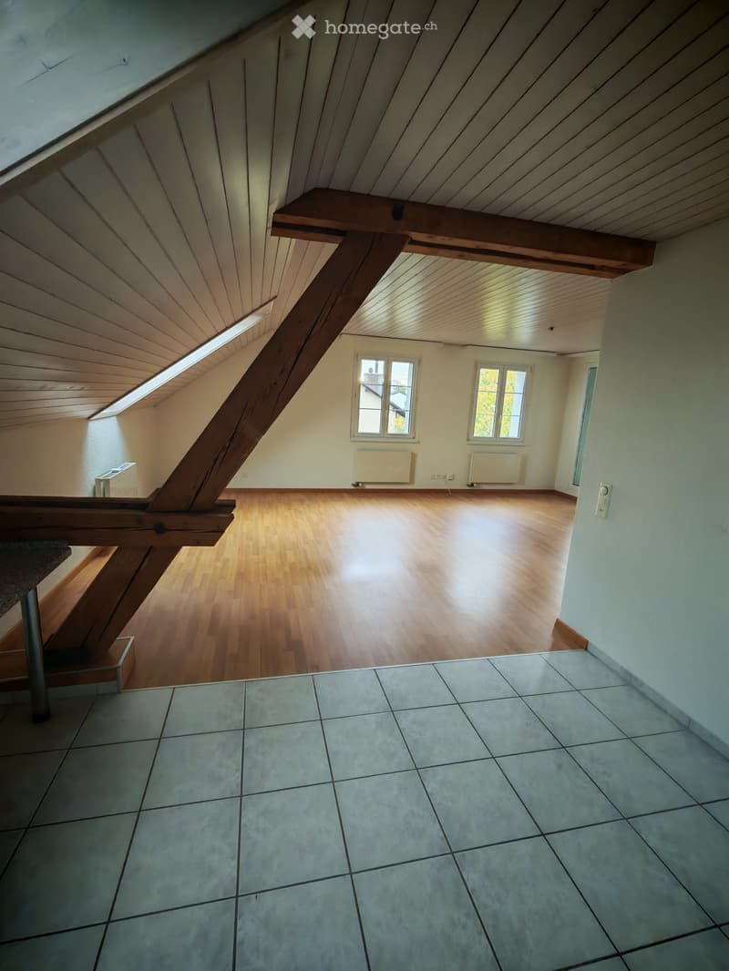 Empty attic space with wooden floors, slanted wooden ceilings, skylight, and windows. No furniture or equipment present.