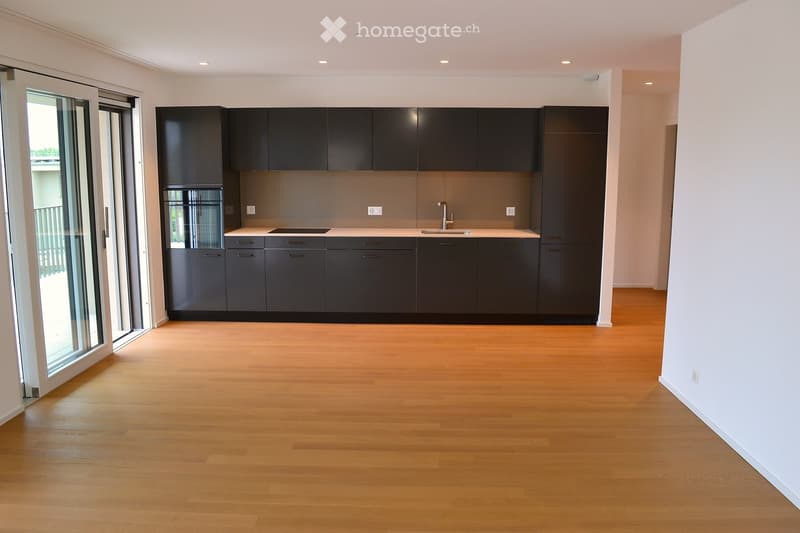 Modern kitchen with dark grey cabinets, white countertops, and a light wooden floor. Features a large sliding glass door leading to a balcony.