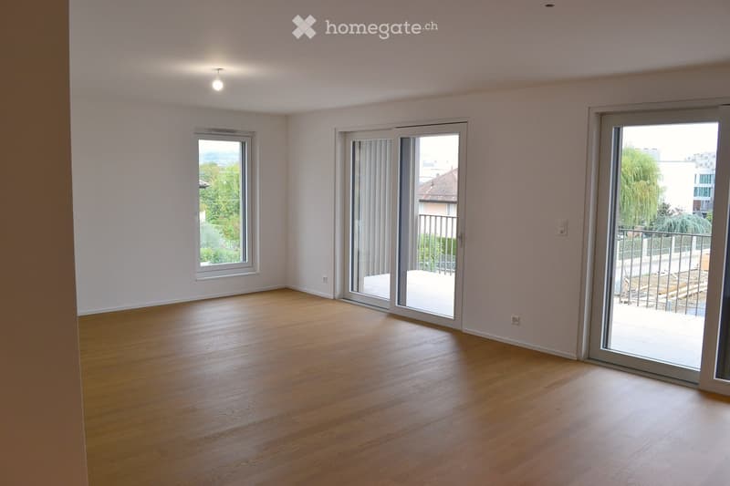 Empty room with wooden flooring, large windows, and sliding glass doors leading to a balcony.