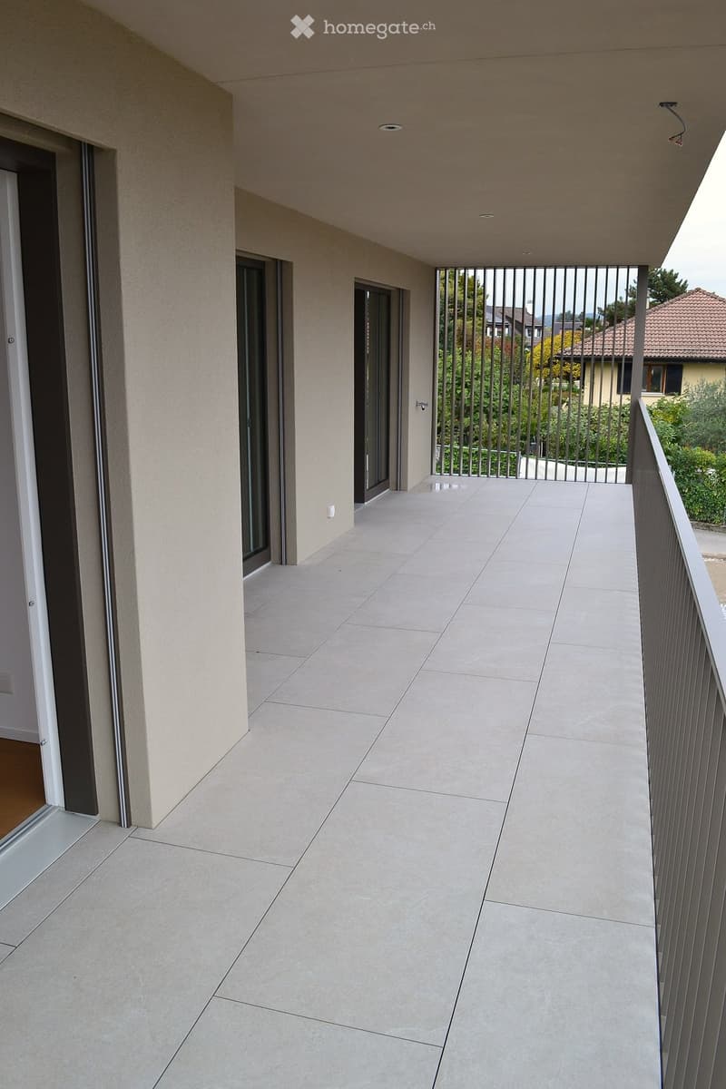 Modern balcony with tiled flooring, metal railing, and glass doors leading to the interior.