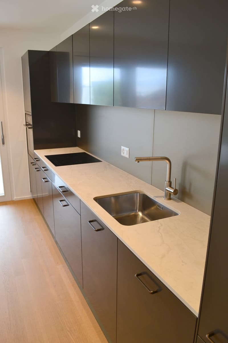 Modern kitchen with sleek grey cabinets, a white marble countertop, a stainless steel sink, and a contemporary faucet.