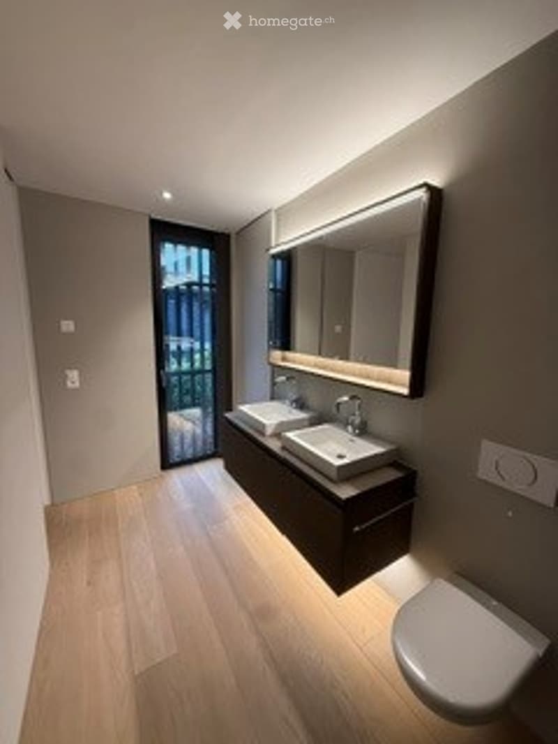 Modern bathroom with dark grey walls, light wooden flooring, double sink vanity, large mirror, and a toilet.