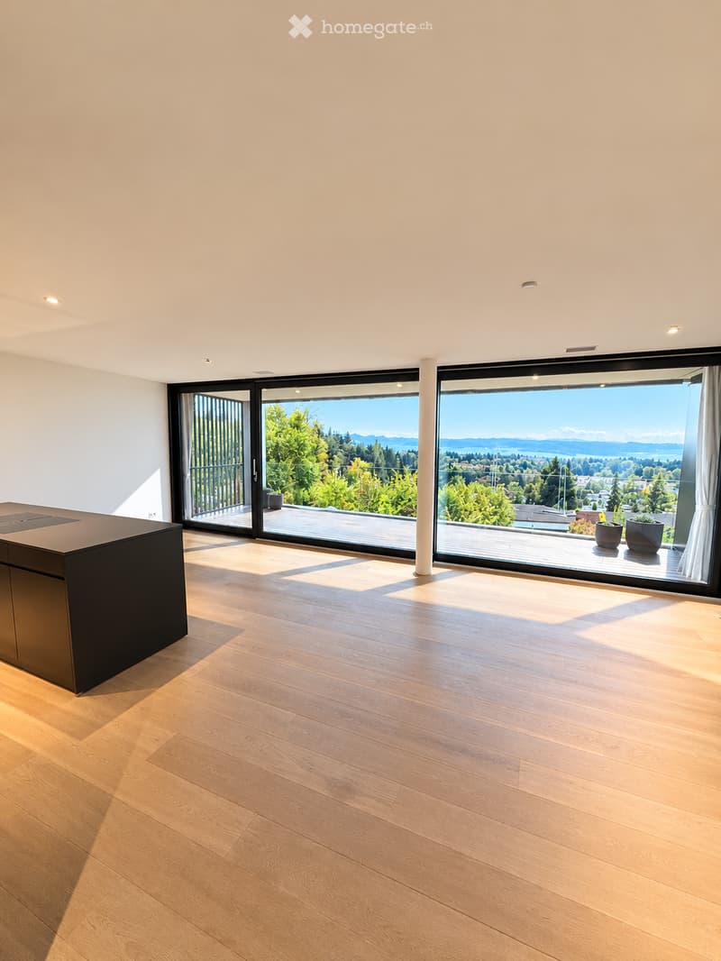 Modern, minimalist kitchen with light wooden flooring, large sliding glass doors leading to a balcony with scenic views, and a sleek black kitchen island.