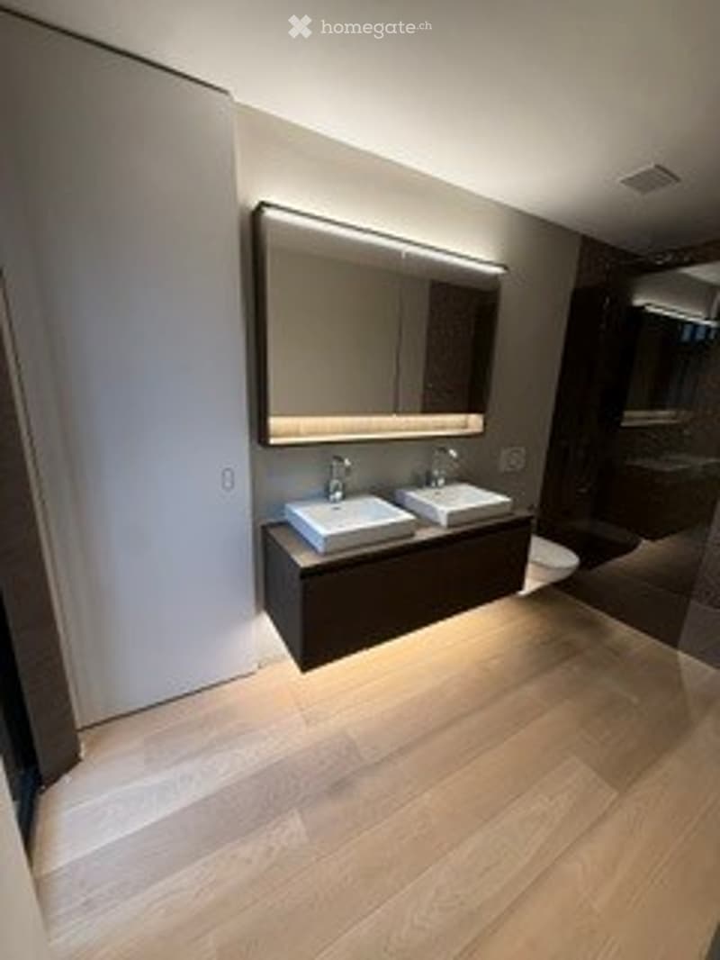 Modern bathroom with a double sink vanity, sleek mirror with built-in lighting, and light wood flooring.