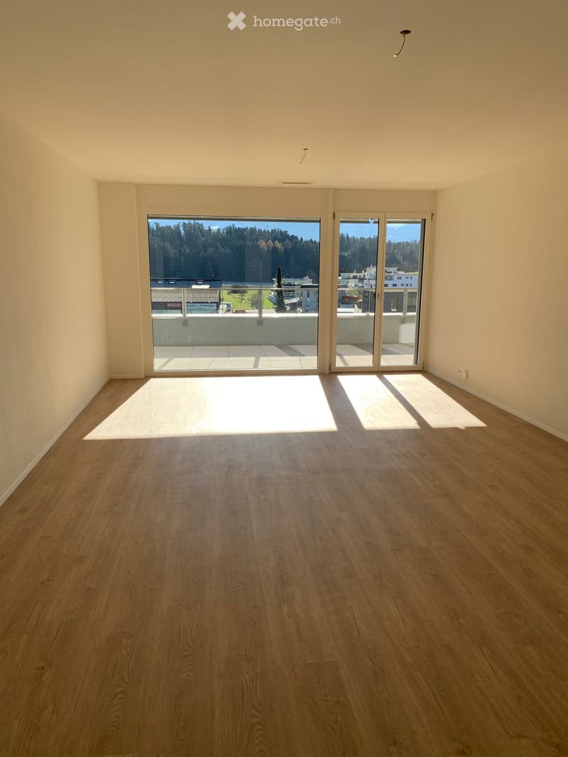 Empty room with wooden flooring and large sliding glass doors leading to a balcony with a scenic view.