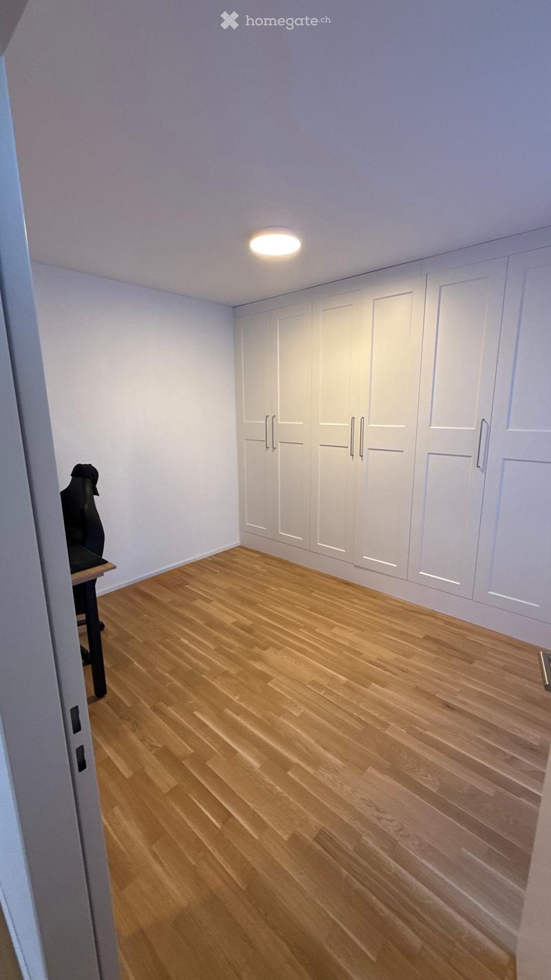 Empty room with light wooden flooring, white walls, built-in wardrobes, and a single ceiling light fixture.