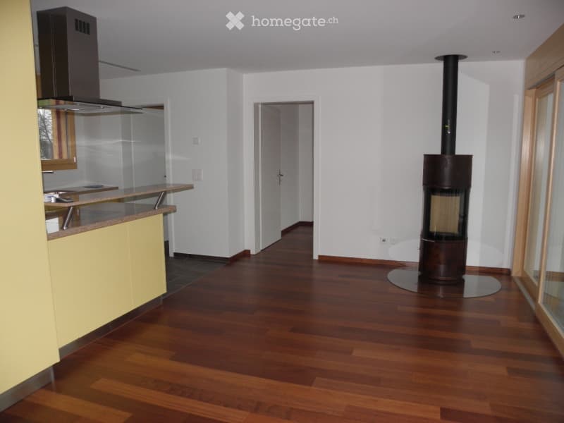 Bright, open-plan living and dining area with wooden flooring, a modern fireplace, and a small kitchen area with cabinets and a counter.