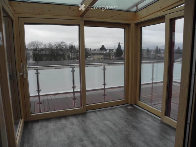 Empty room with large glass doors leading to a balcony or terrace, wooden flooring, and a view of the surrounding area.