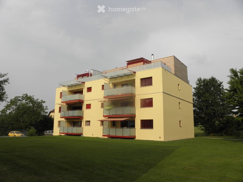 Modern multi-story residential building with balconies, yellow facade, and red accents.