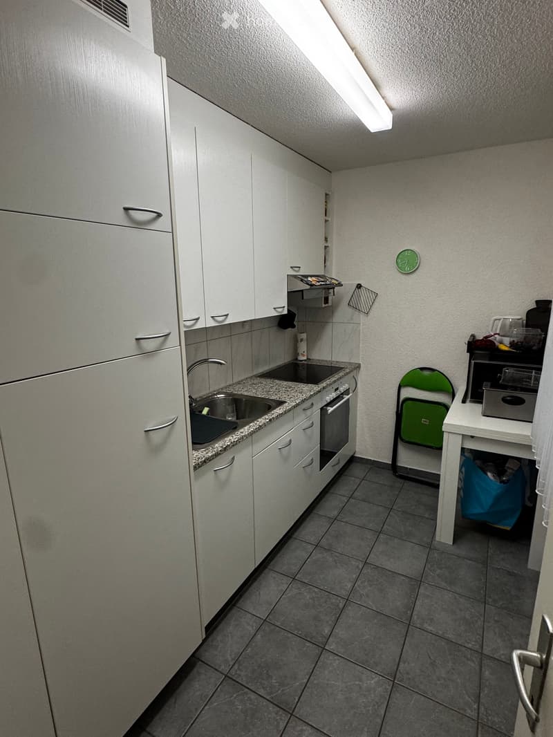 Modern kitchen with white cabinets, granite countertop, sink, oven, and a small table with a chair.