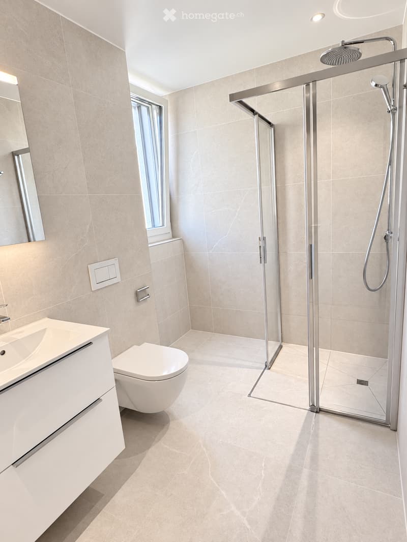 Modern bathroom with beige tiles, a white sink, toilet, and a glass-enclosed shower with a modern showerhead.